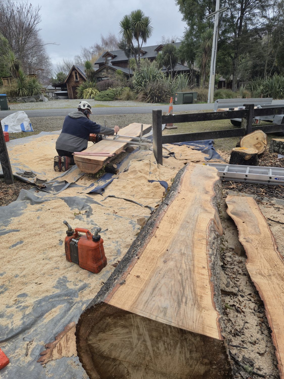 A log being cut into slabs with a chainsaw mill on a tarp, sawdust all round and a fresh slab in the foreground